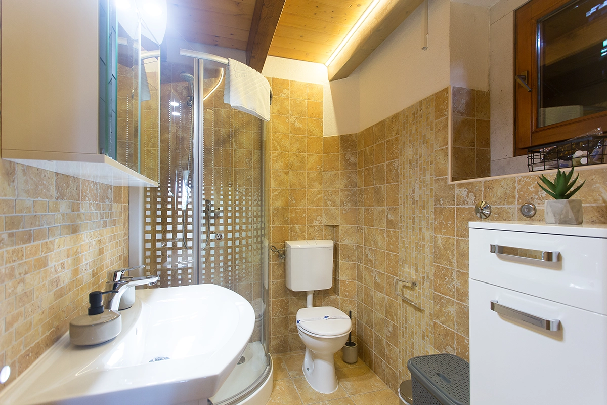 Bathroom with a sink, toilet, shower cabin, cabinet, and brown tiles.